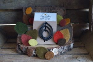 Needle felted leave in autumnal colours surrounding the beech leaf template set with rustic wooden background