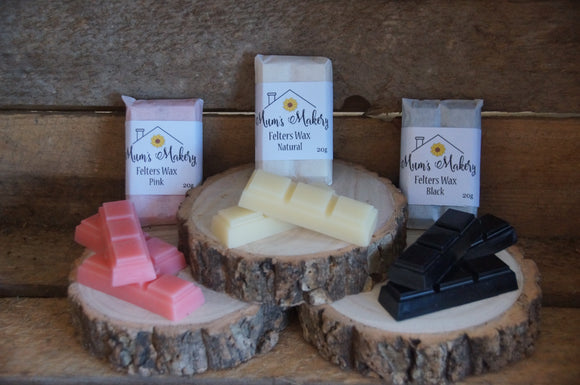 Needle Felters Wax in Natural, Pink and Black 3 square bars displayed on little log slices with a rustic wooden background